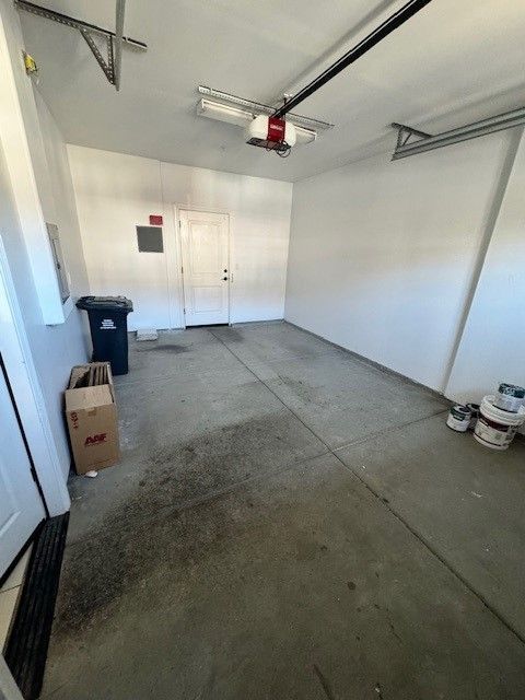 A garage with a garage door open and a bucket of paint on the floor.