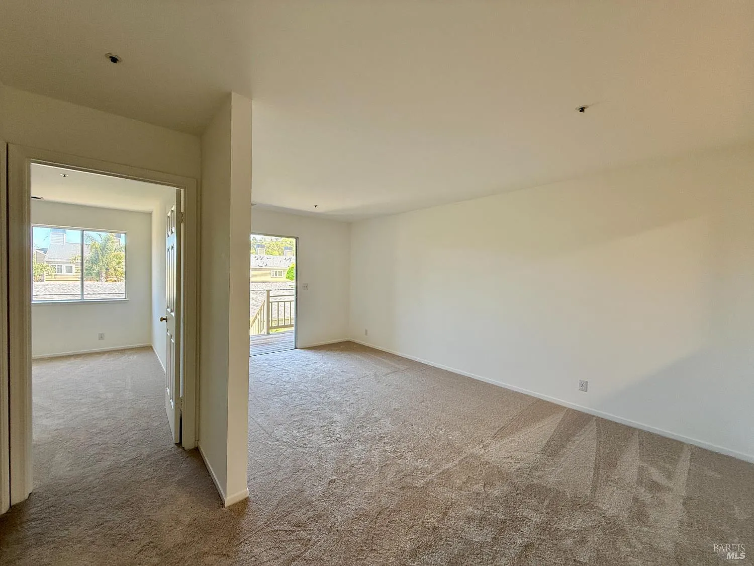 Empty beige apartment interior with carpeted living room, hallway, and bright windows