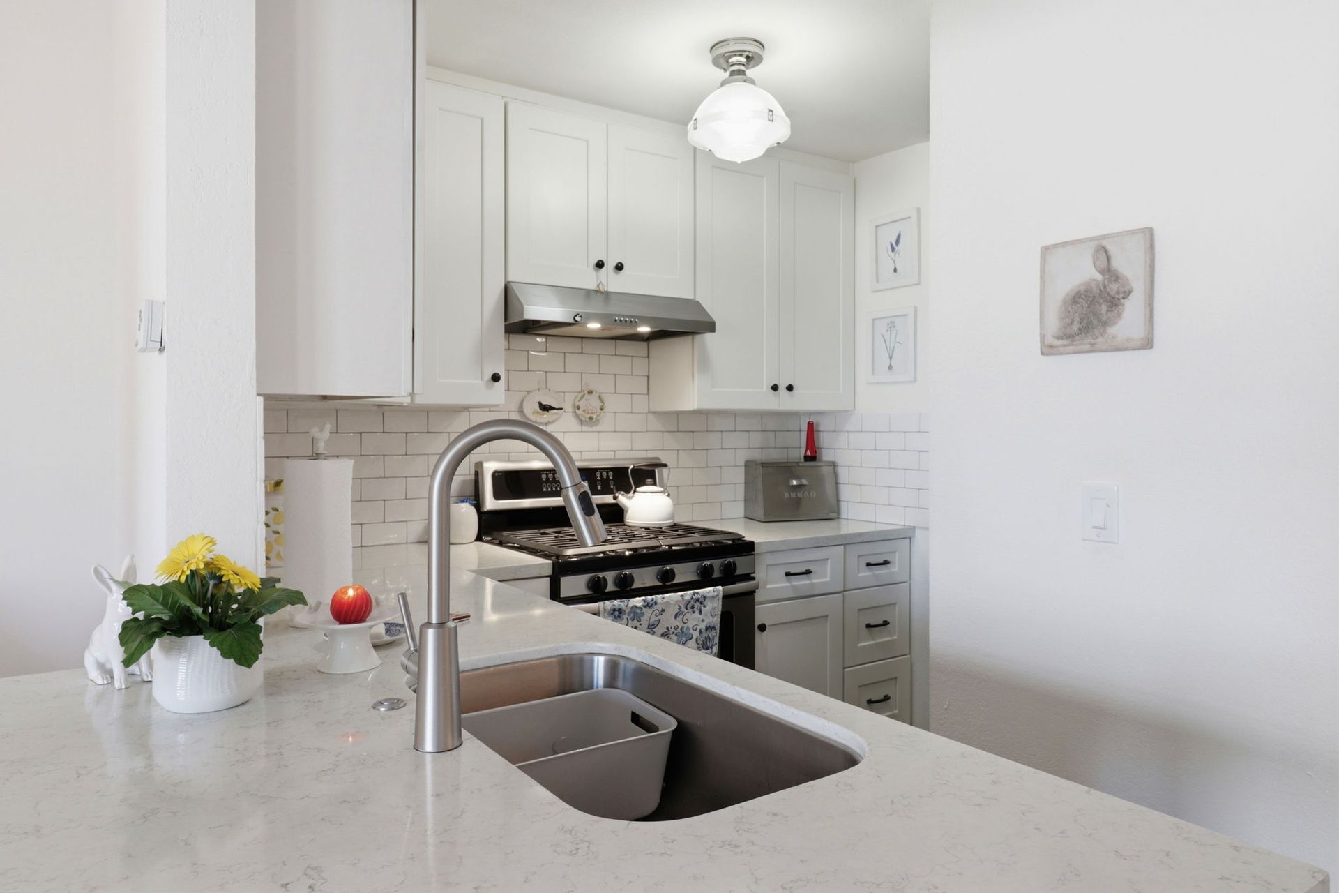 Bright white kitchen with island sink, gas stove, and vase of flowers