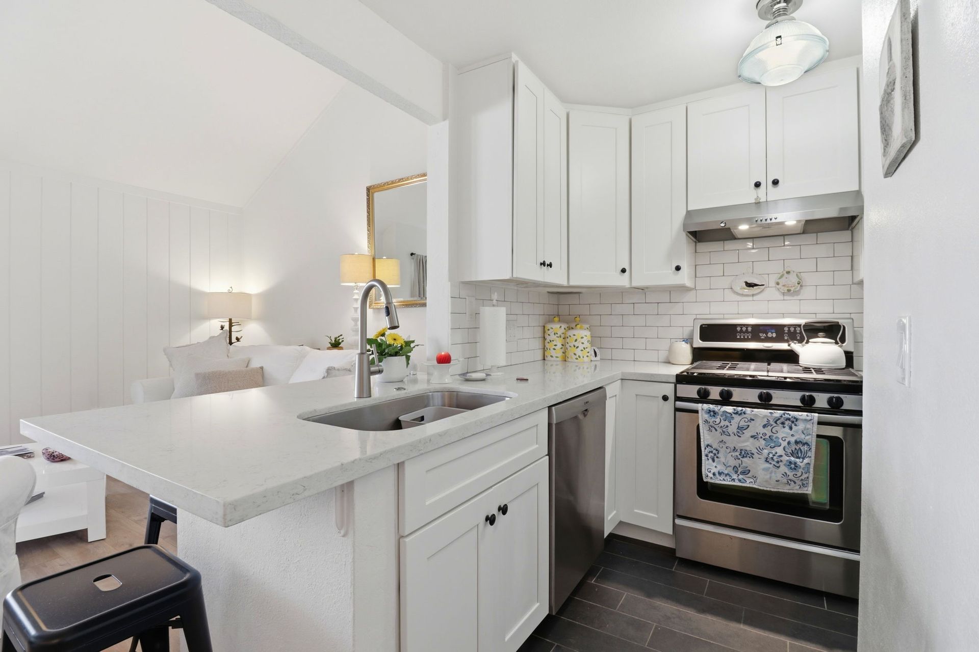 Bright white kitchen with island, stainless steel stove, and a small dining area by a bed