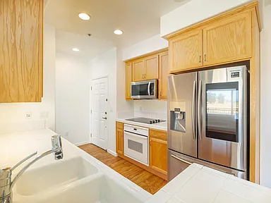 A kitchen with light wood cabinets, stainless steel refrigerator, white appliances, and sink.