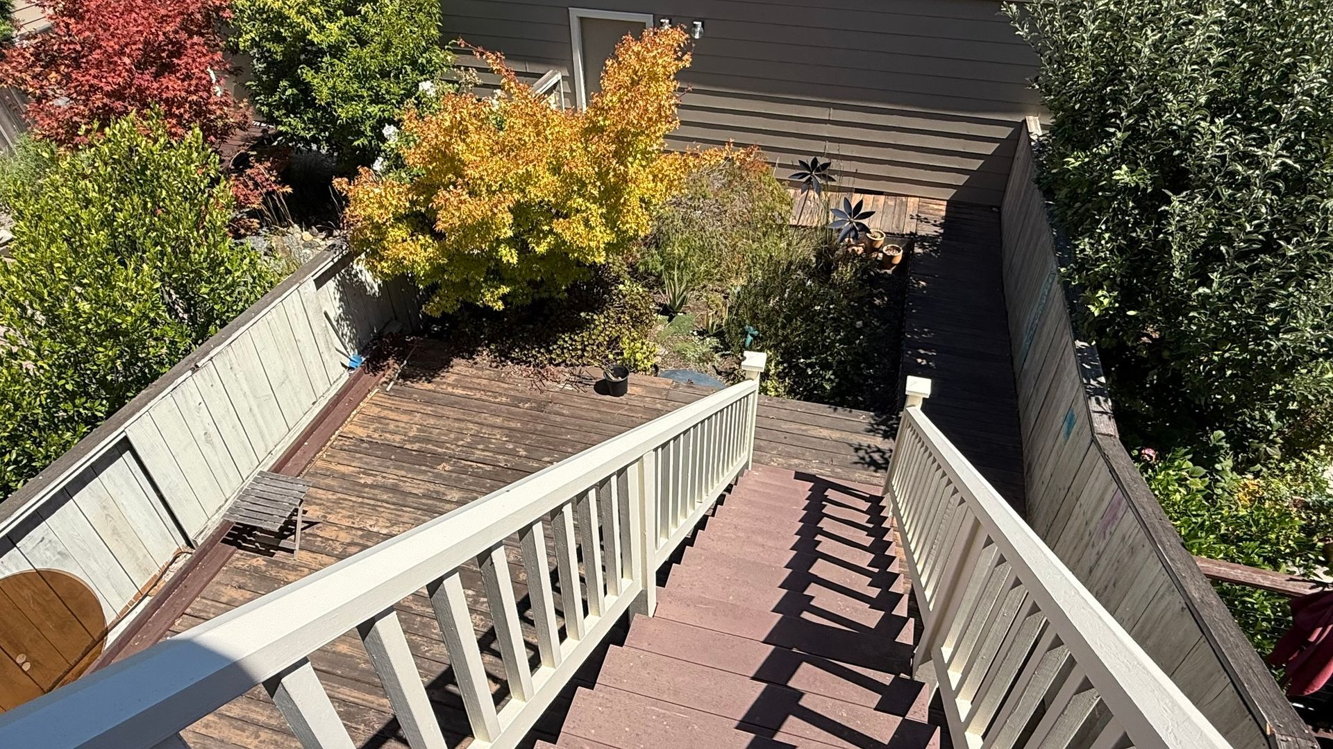 Steep rooftop stairway with white railings leading to a lower roof and trees in the background