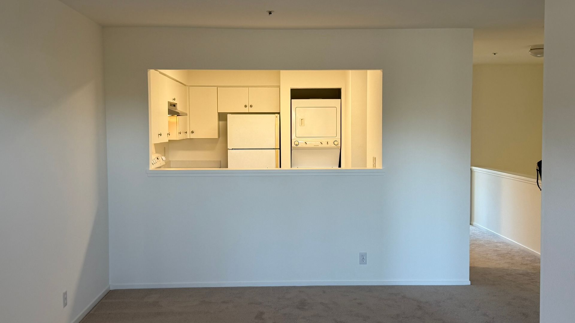 Empty living room with a pass-through view into a bright kitchen area.