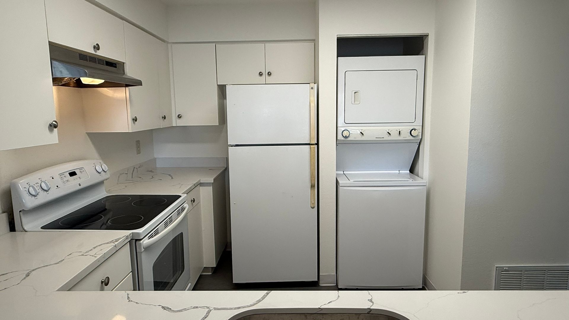 Small beige kitchen with white appliances, cabinets, stove, refrigerator, and stacked washer-dryer.