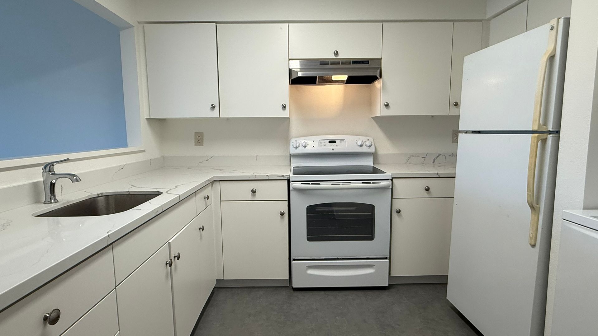 White kitchen with stove, refrigerator, sink, and white cabinets along the walls.