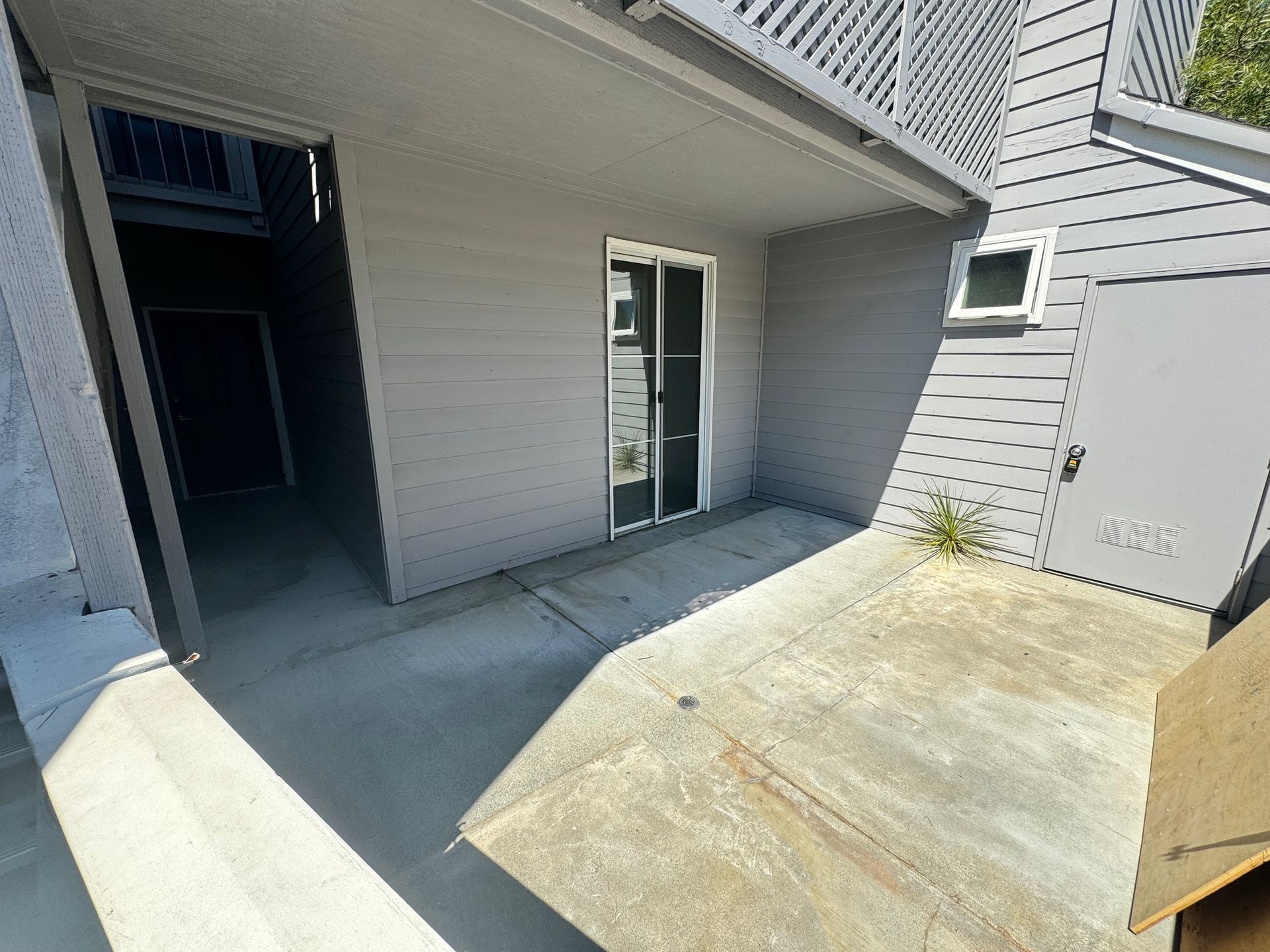 A patio with a sliding glass door and a concrete floor in front of a building.