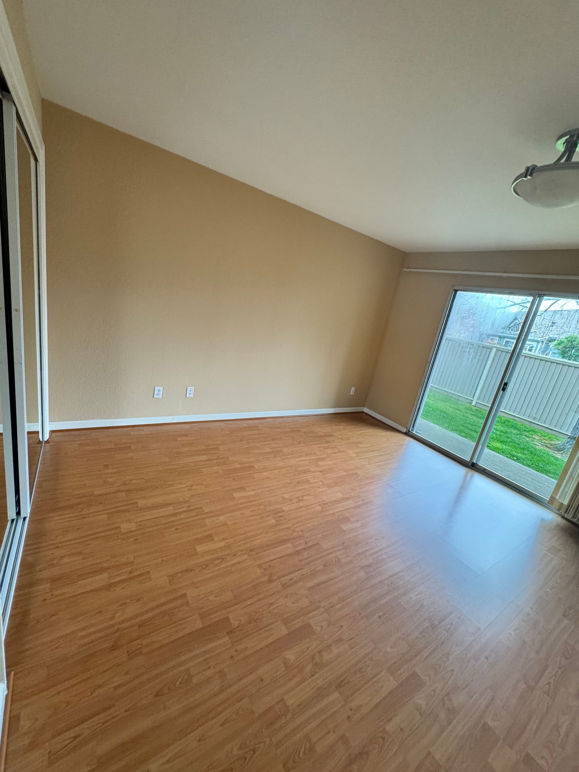 An empty living room with hardwood floors and sliding glass doors.