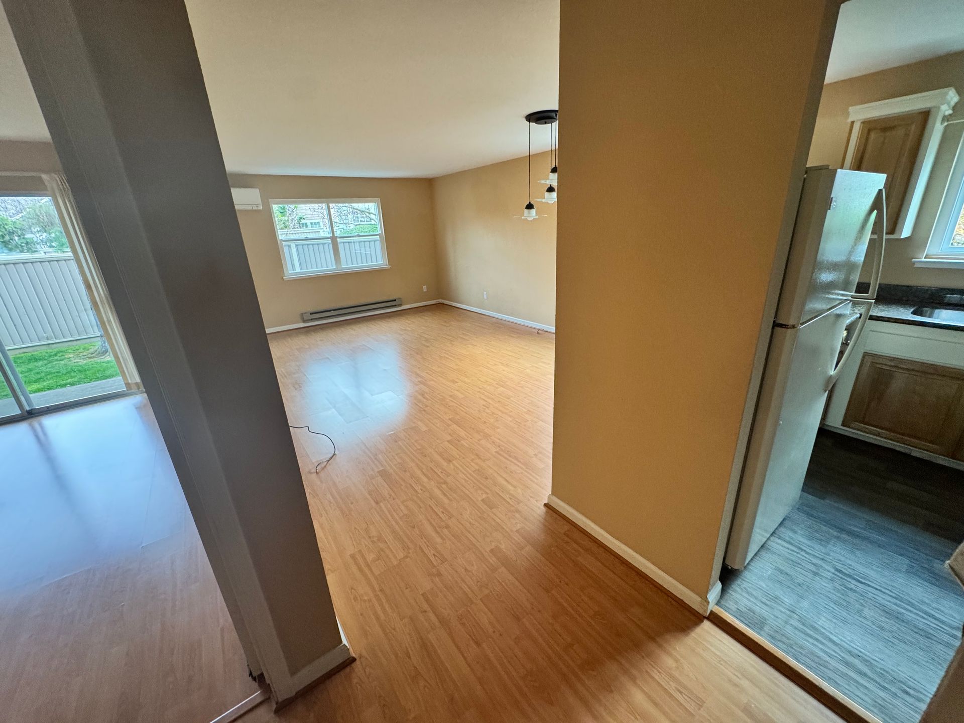 A living room with hardwood floors and a refrigerator in a house.