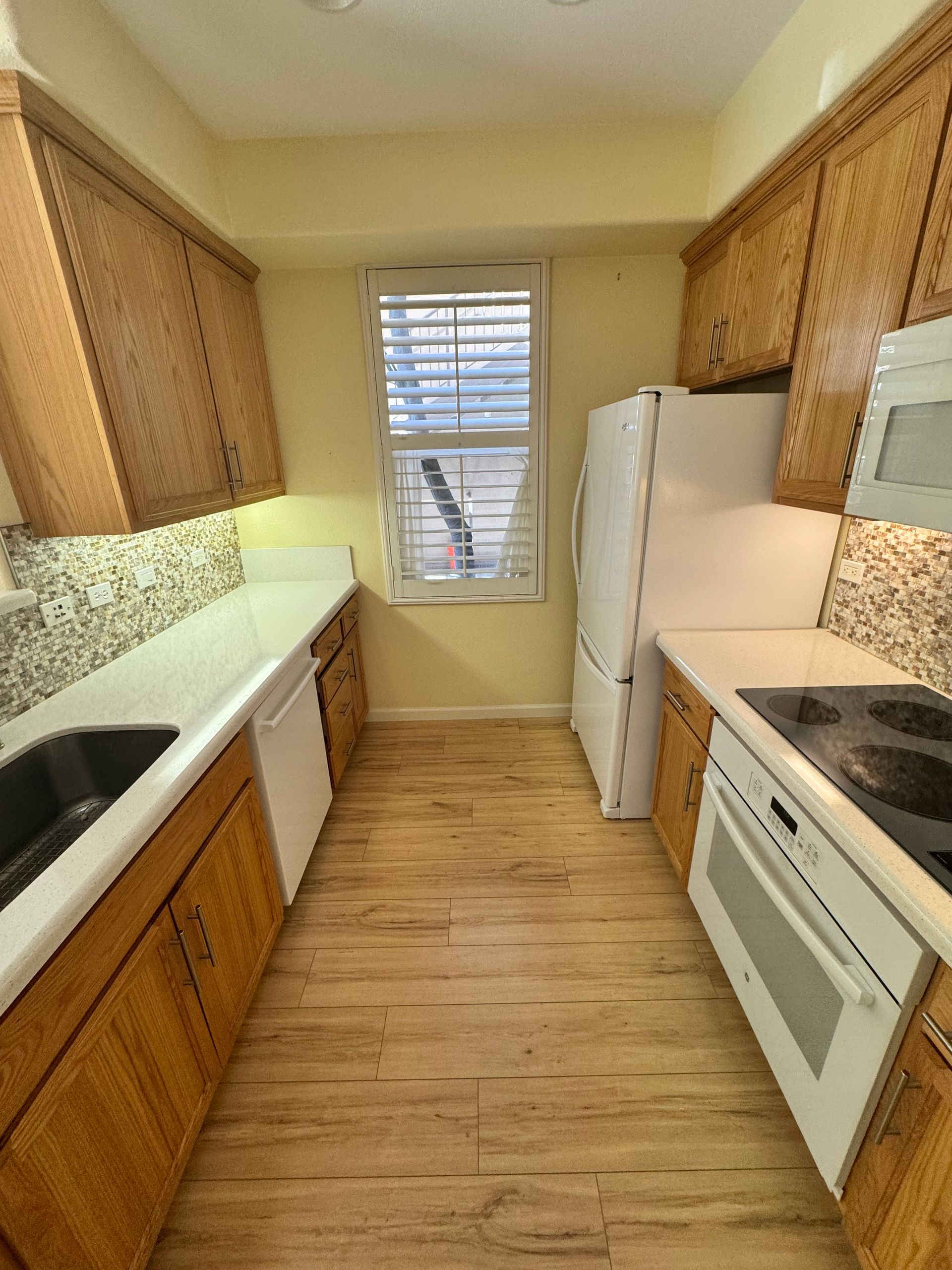 A kitchen with wooden cabinets , white appliances , a sink and a refrigerator.