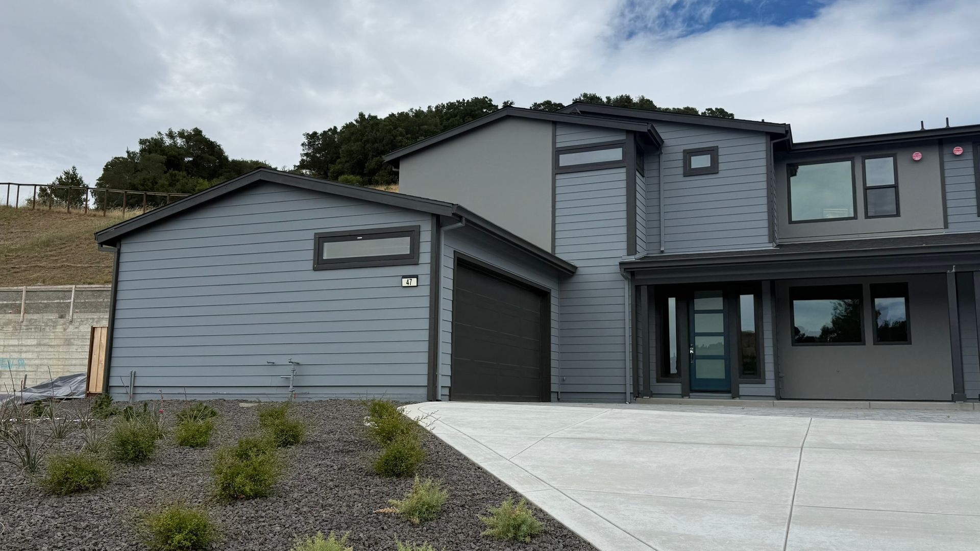 Modern gray two-story house with attached garage and concrete driveway under a cloudy sky