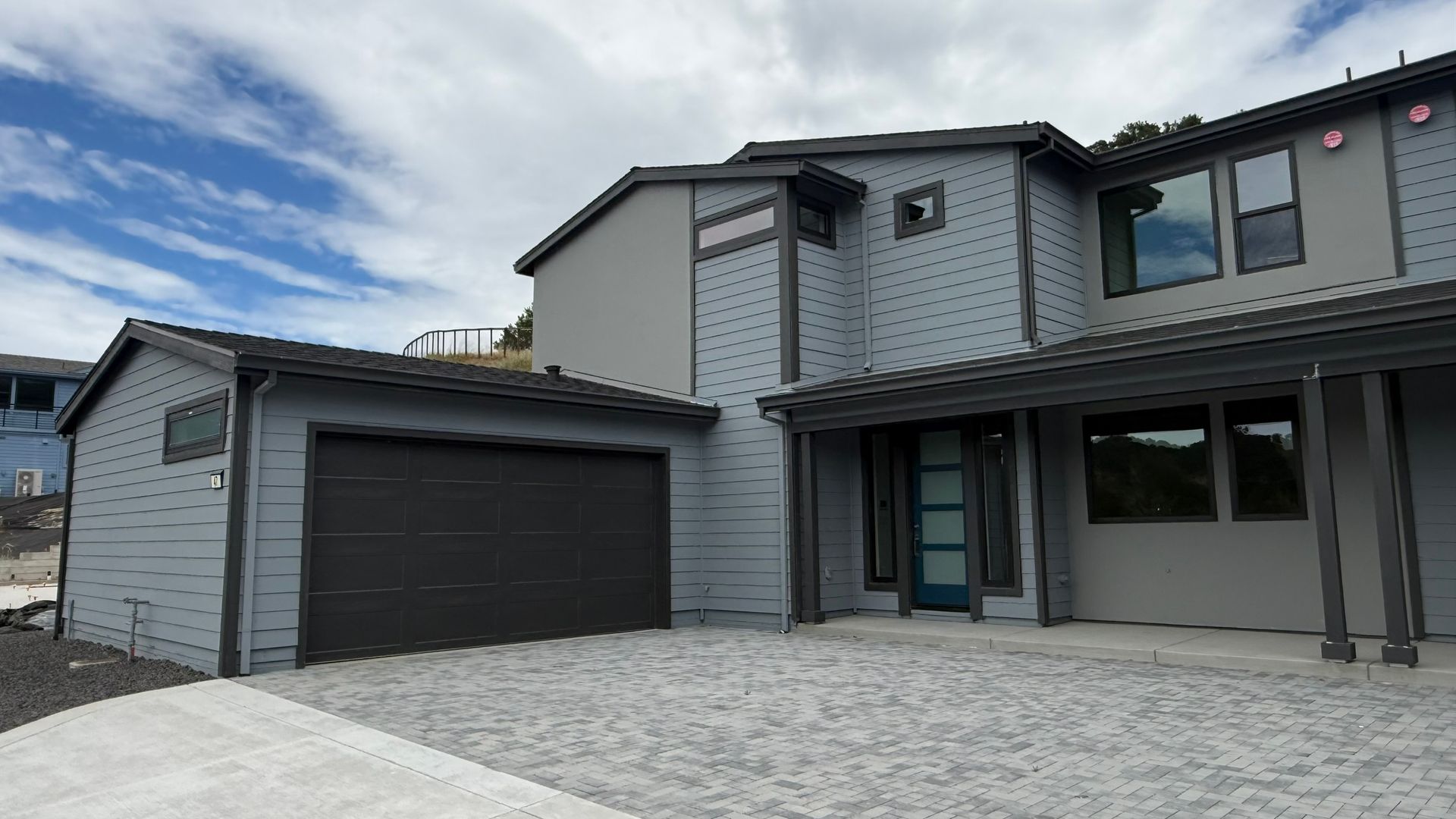 Modern two-story gray house with a dark garage and covered front porch under a cloudy sky