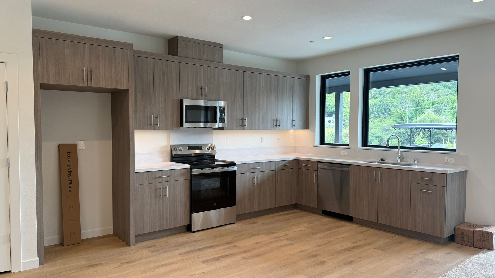 Modern kitchen with wood cabinets, black appliances, white backsplash, and large windows overlooking greenery
