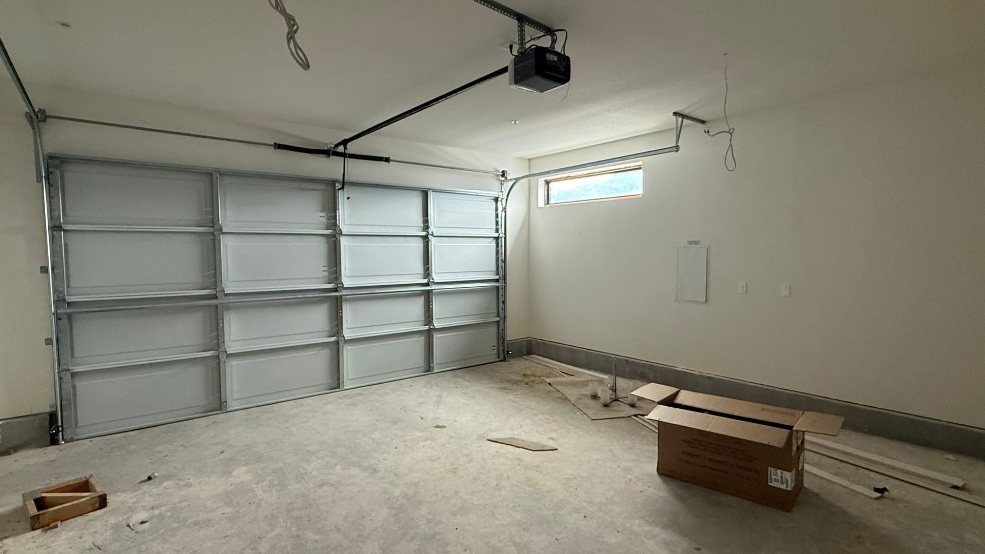 Empty garage interior with a closed sectional door, unfinished floor, and a few boxes on the right.