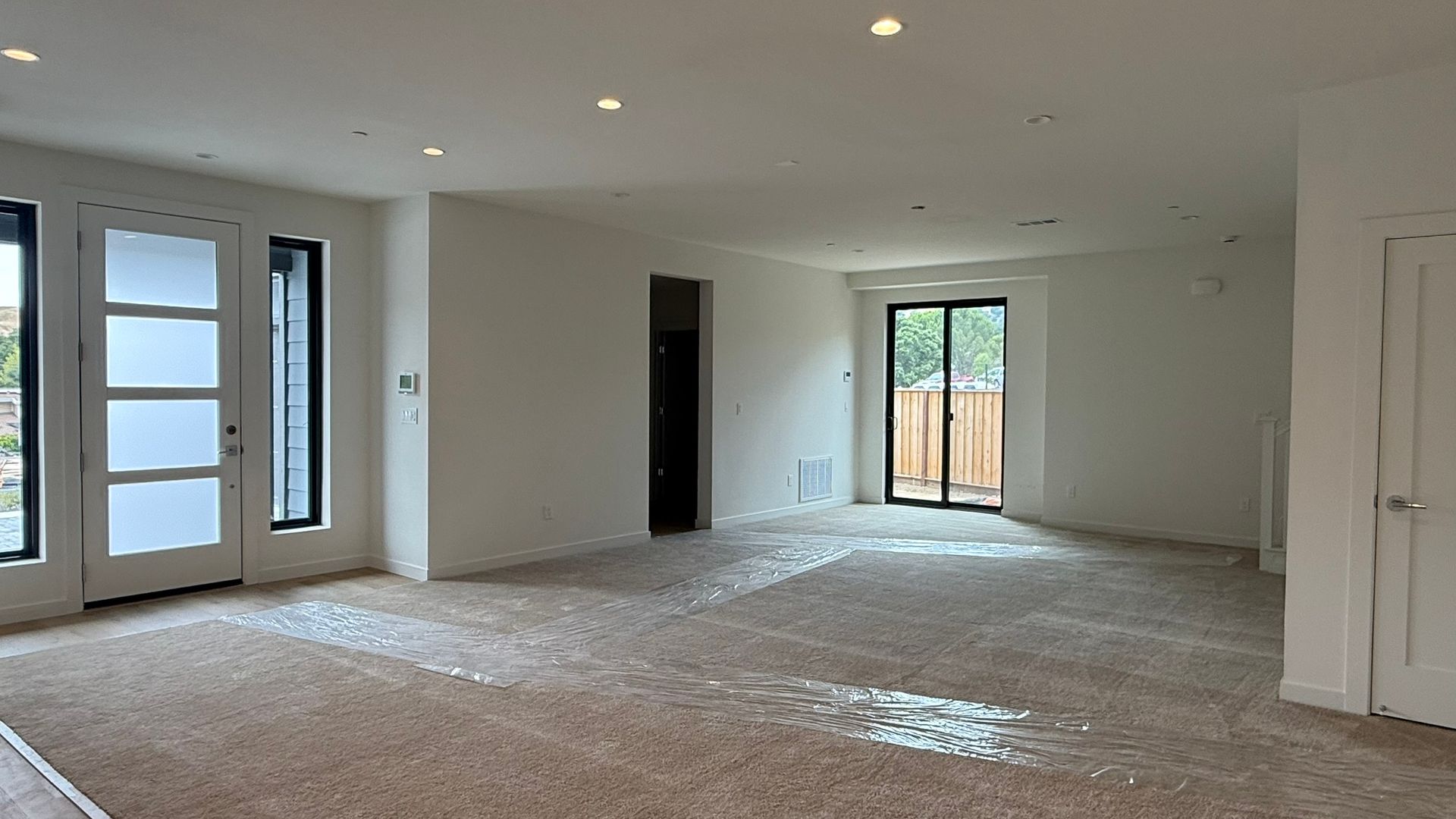 Empty unfinished living room with carpet, recessed lights, and large windows and glass door.