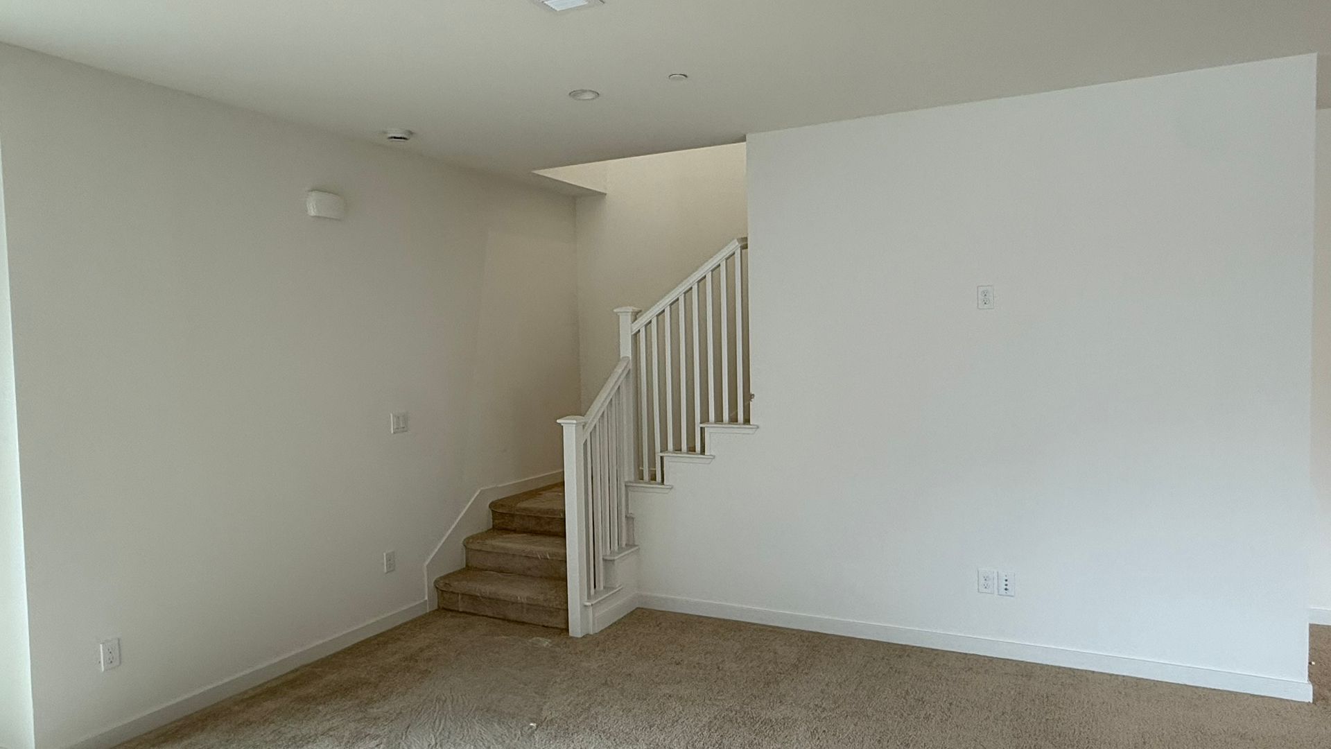 Empty living room with carpeted stairs and a white railing leading to an upper level