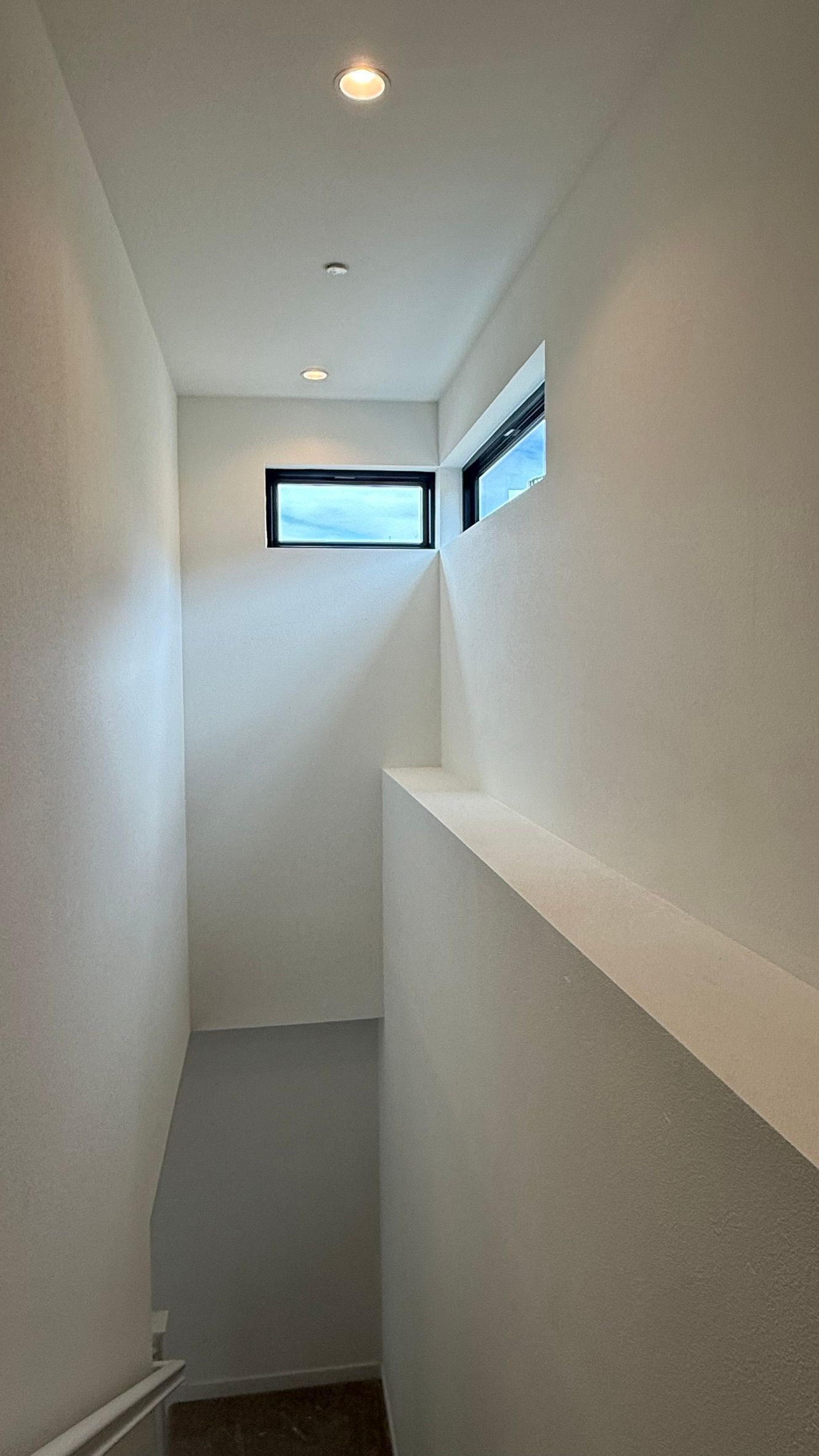 Narrow white hallway with a small high window and recessed ceiling lights.
