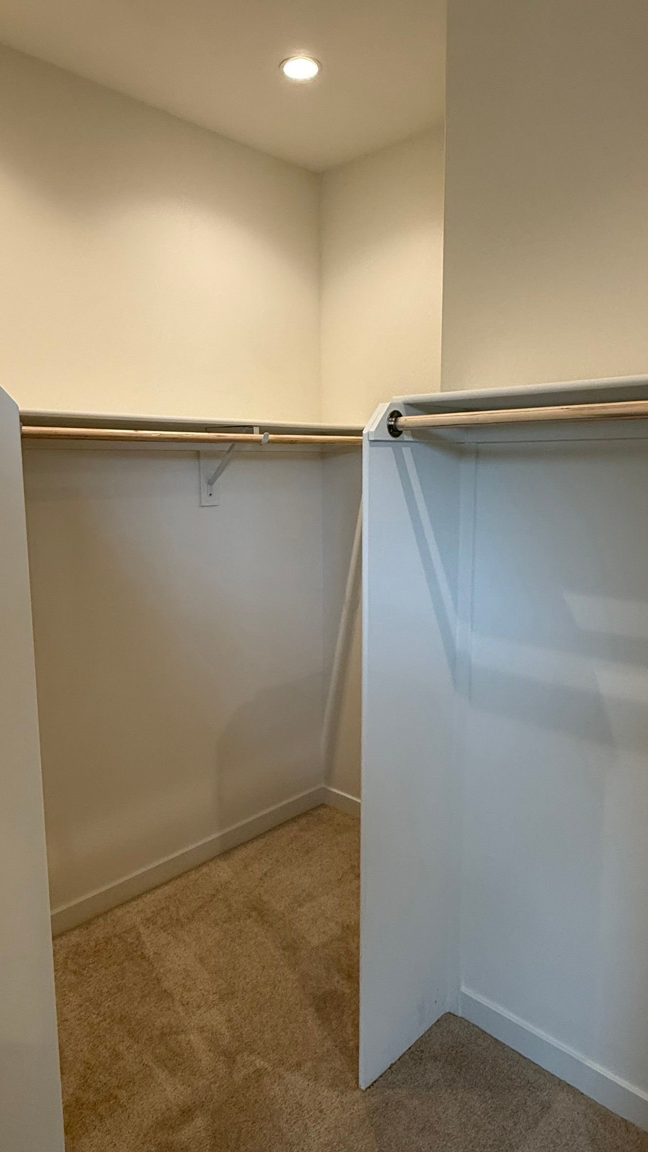 Empty closet with beige carpet, white walls, and a hanging rod on each side.