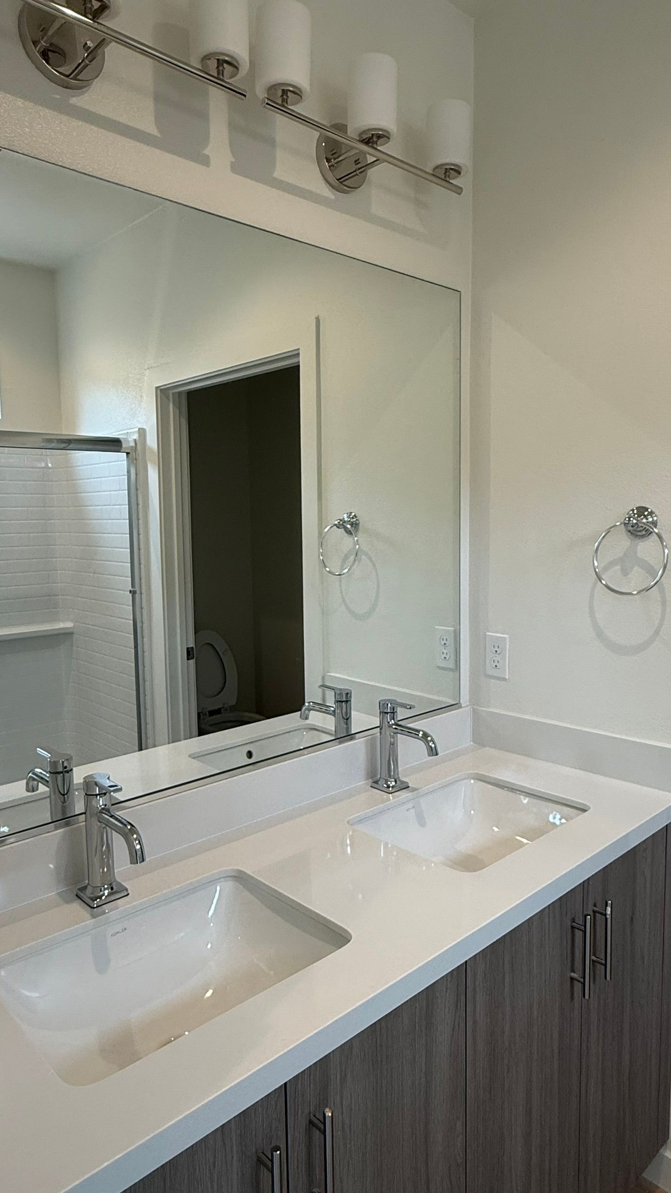 Bathroom vanity with double sinks, large mirror, and wood cabinets under bright lighting
