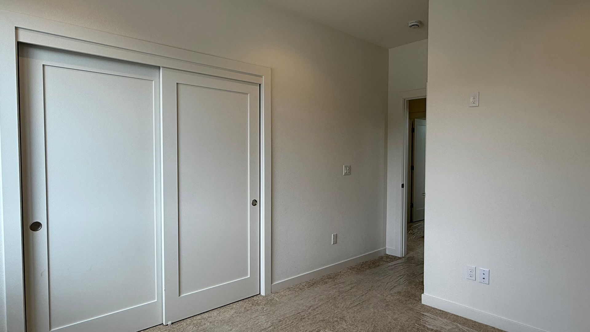 Empty beige bedroom with sliding closet doors and carpeted floor