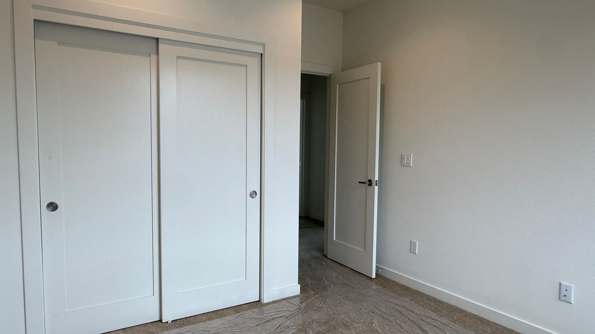 Empty beige bedroom with white closet doors, open doorway, and carpeted floor.