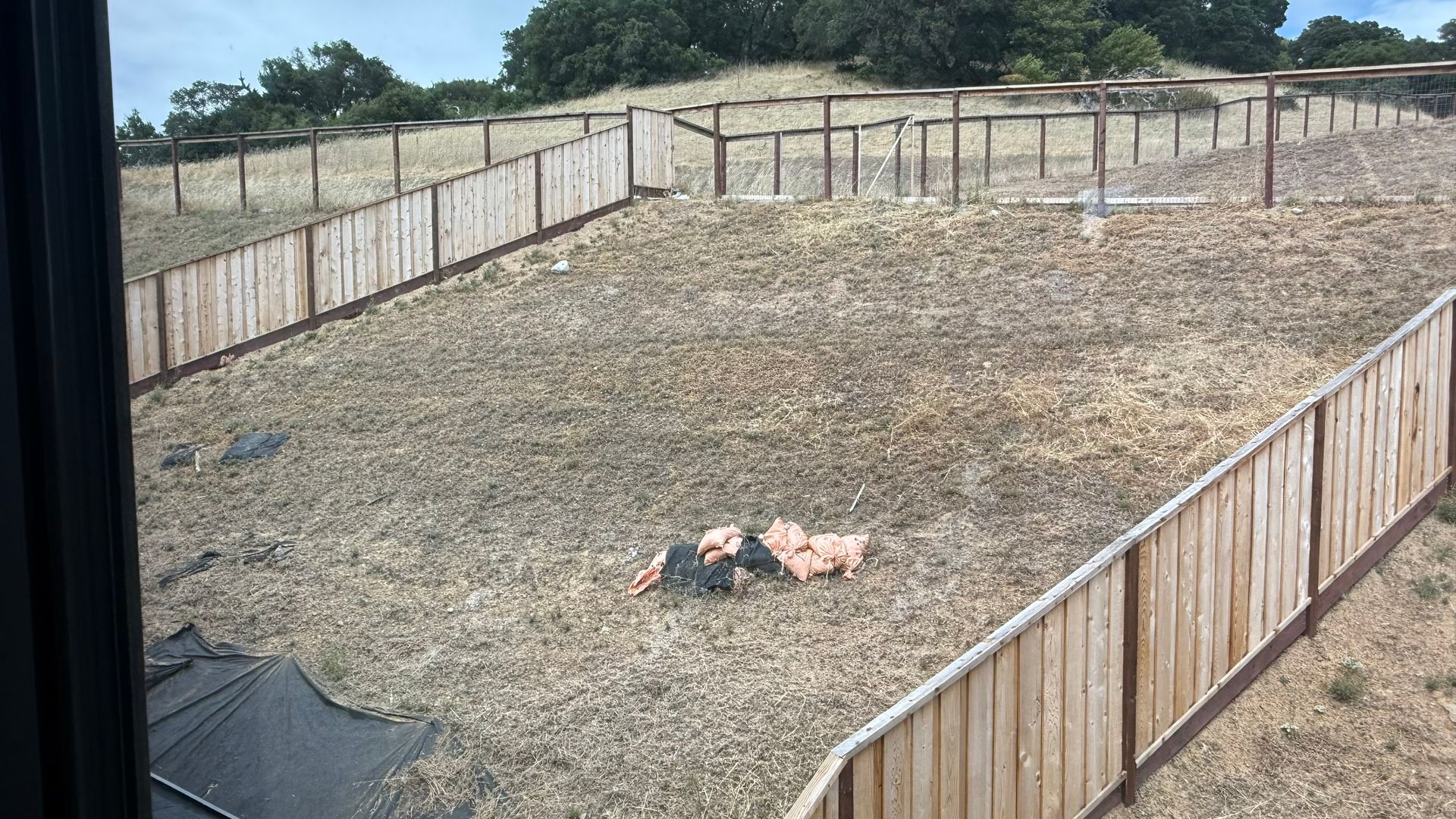Wide fenced dirt yard with a dog lying in the center, viewed from above