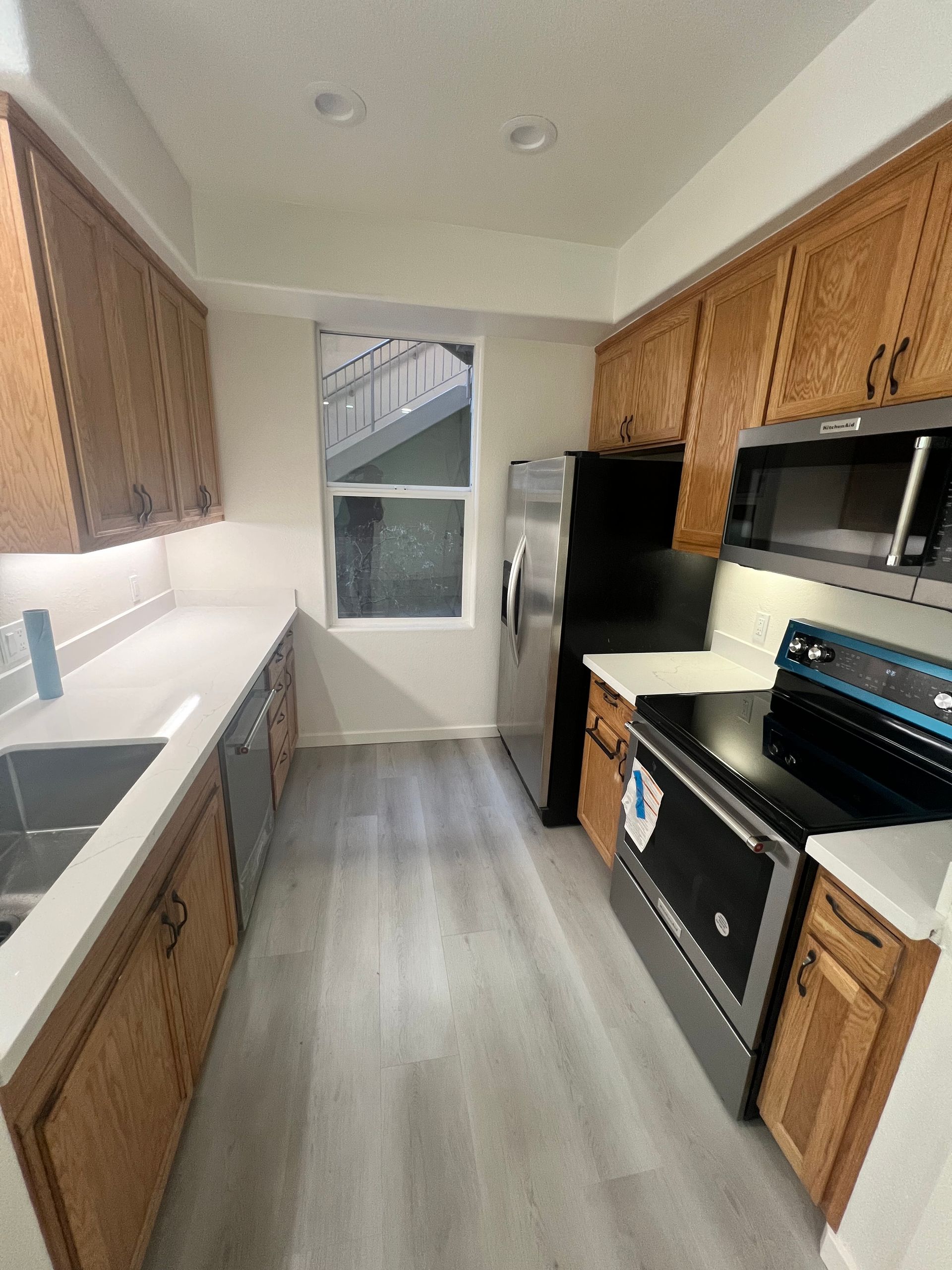 A kitchen with wooden cabinets , a stove , a refrigerator , a microwave , and a sink.