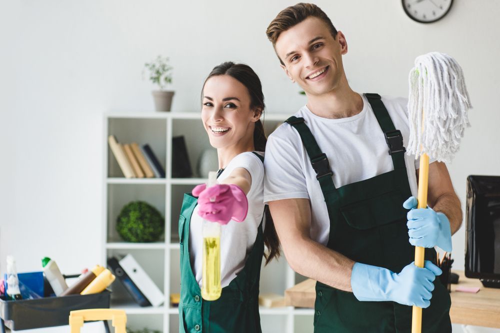 Smiling Man and Woman Holding Cleaning Supplies — Cleaners in Tamworth, NSW 