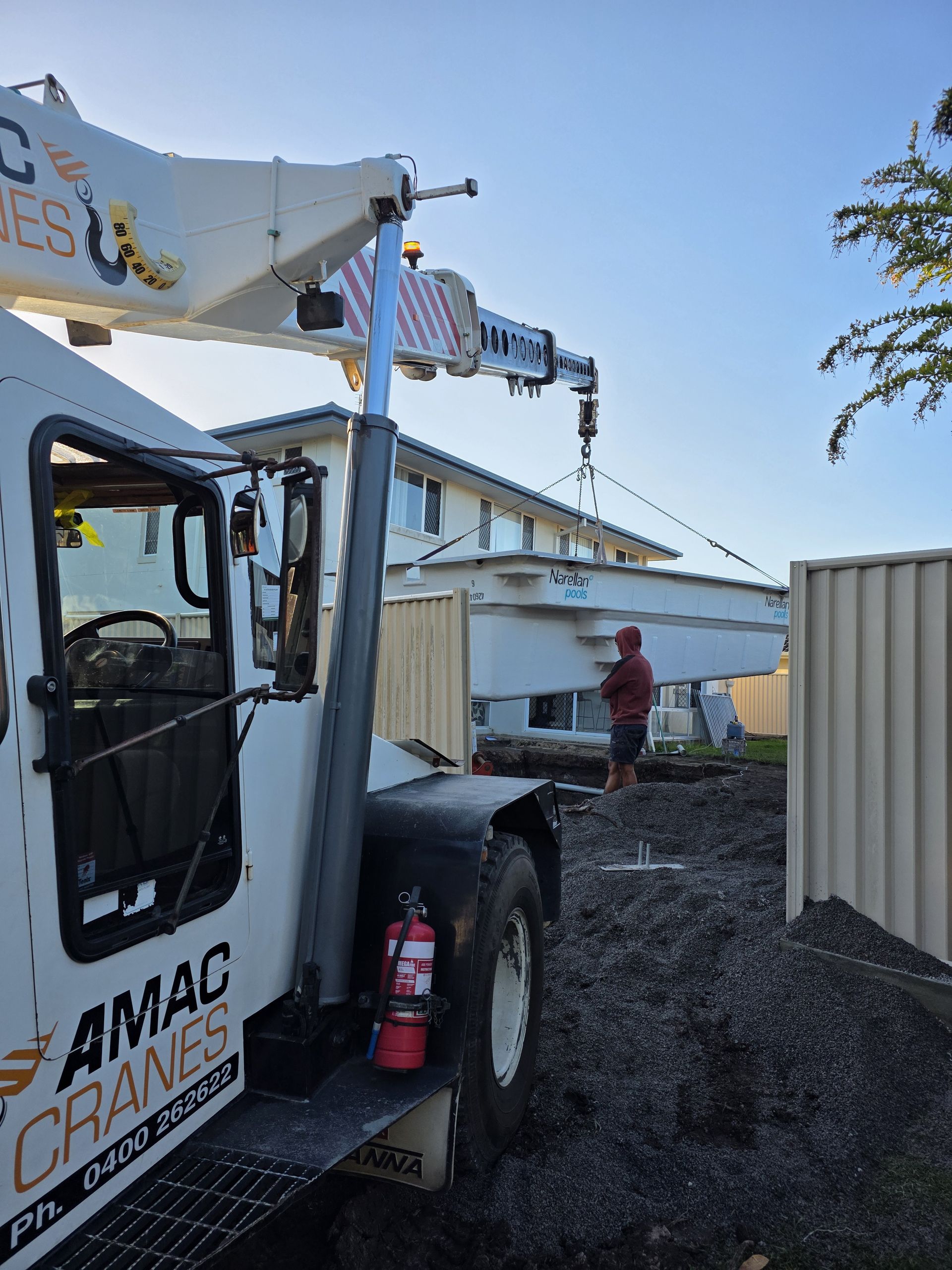 A Construction Worker Is Standing Next to A White Crane at A Construction Site — AMAC Cranes in Coolum Beach, QLD