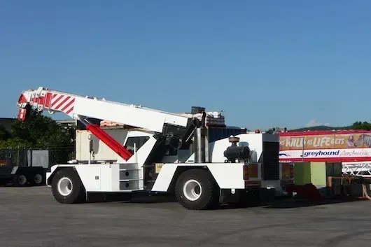 A White Crane Is Parked in A Parking Lot Next to A Sign that Says' Mardi Gras' — AMAC Cranes in Coolum Beach, QLD