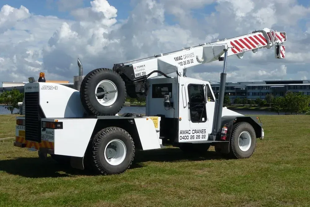 A White Truck with A Crane on The Back Is Parked in A Grassy Field — AMAC Cranes in North Lakes, QLD