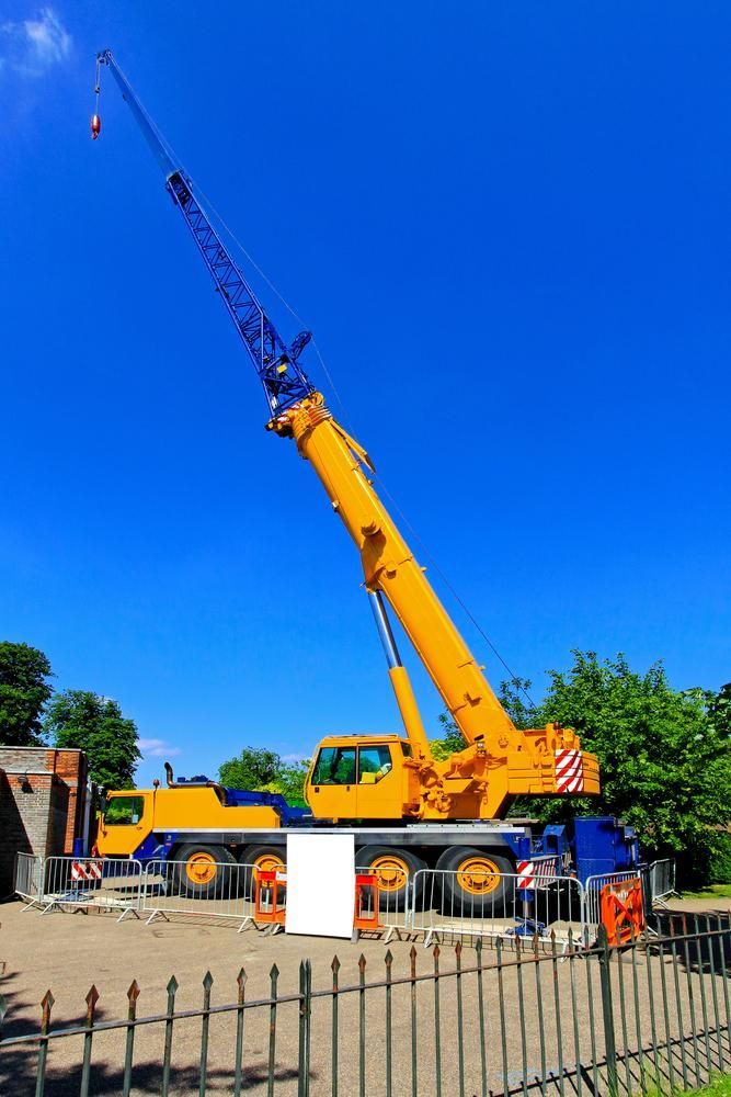 A Large Yellow Crane Is Parked in Front of A Fence on A Construction Site — AMAC Cranes in Coolum Beach, QLD