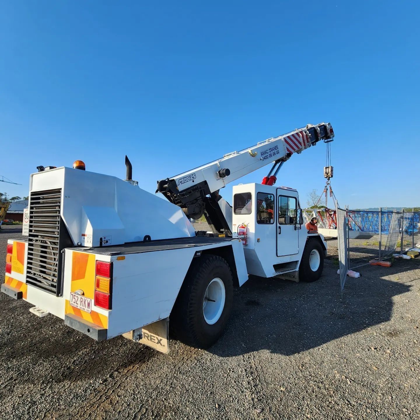 A white mobile crane parked on a gravel lot under a clear blue sky.
