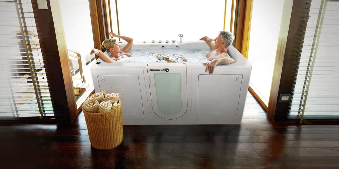 A man and a woman are taking a bath in a walk in tub.