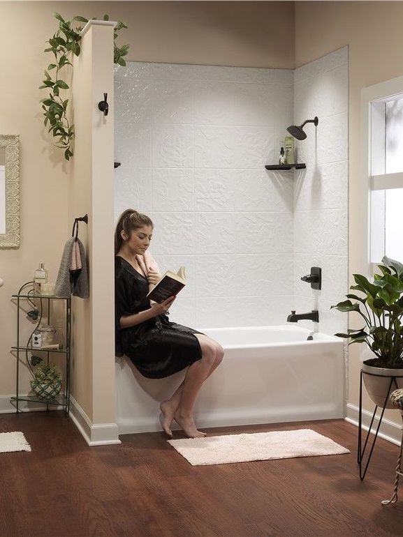 A woman is sitting on the edge of a bathtub reading a book.