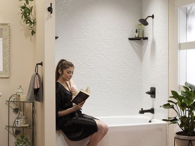 A woman is sitting on a bathtub reading a book.