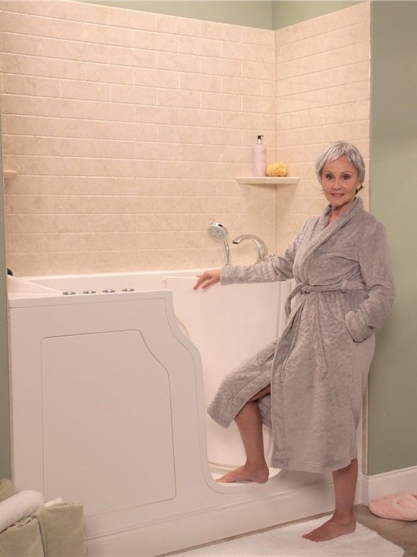 A woman in a bathrobe is sitting in a walk in tub.