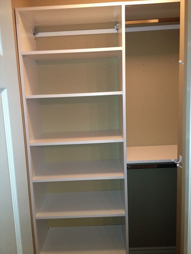Empty white closet with shelves on the left and hanging space on the right, with a dark suitcase below.