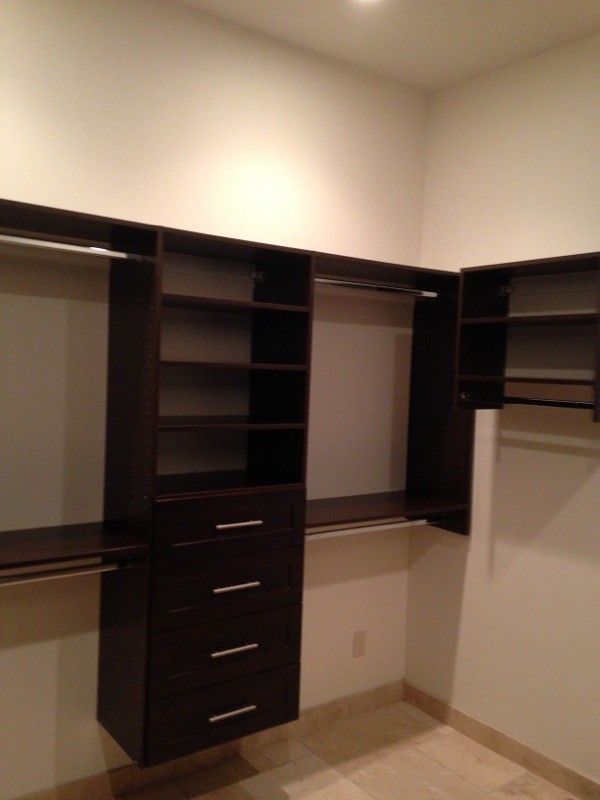Walk-in closet with dark wood shelving, hanging rods, and a center drawer unit