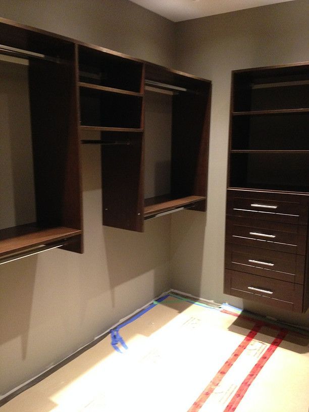 Empty walk-in closet with dark wood shelving, drawers, and hanging space under warm lighting.