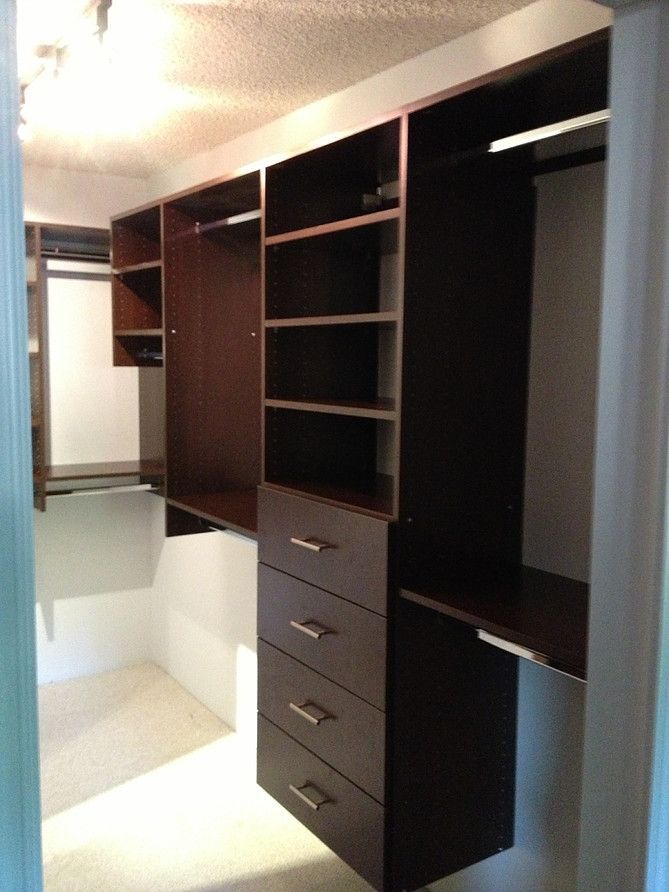 Walk-in closet with dark wood shelves, drawers, and hanging rods built into a white room.