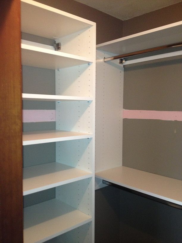 Empty walk-in closet with white shelving and hanging rods on gray walls