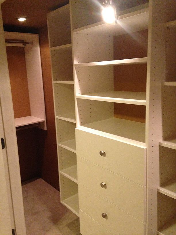 Walk-in closet with built-in white shelves, drawers, and hanging space under warm lighting