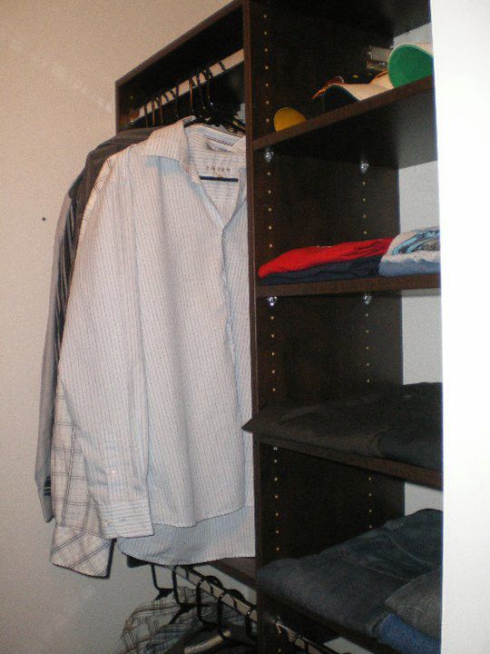 Closet with a striped shirt hanging beside dark shelves holding folded clothes and hangers