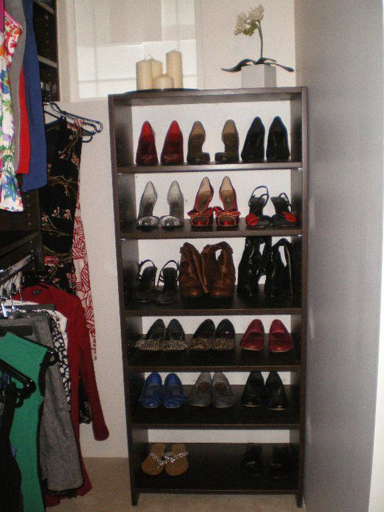 Closet shelf filled with assorted high heels and boots, with clothes hanging on the left.