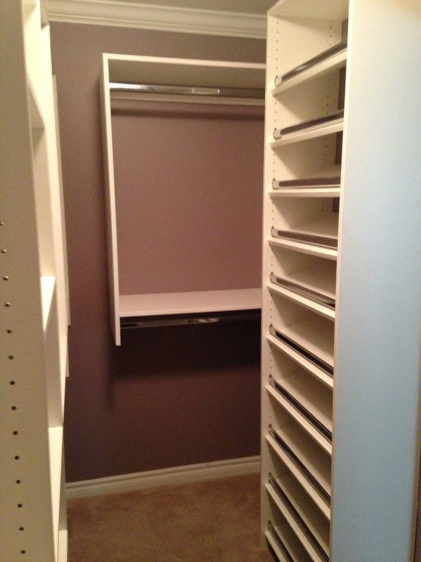 Walk-in closet with beige walls and white shelving, showing hanging clothes and empty shelves.