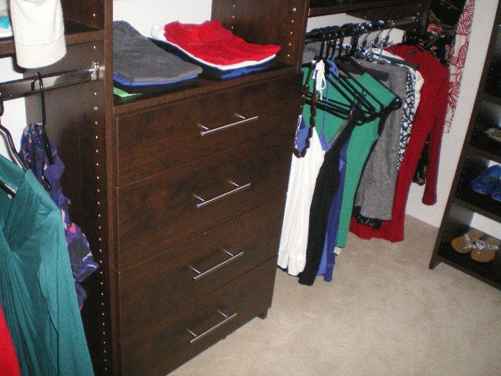 Open closet with hanging clothes, a dark dresser, and folded clothes on shelves.