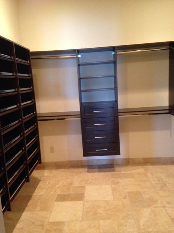 Empty walk-in closet with beige tile floor, dark shelving, hanging rods, and a central drawer unit.