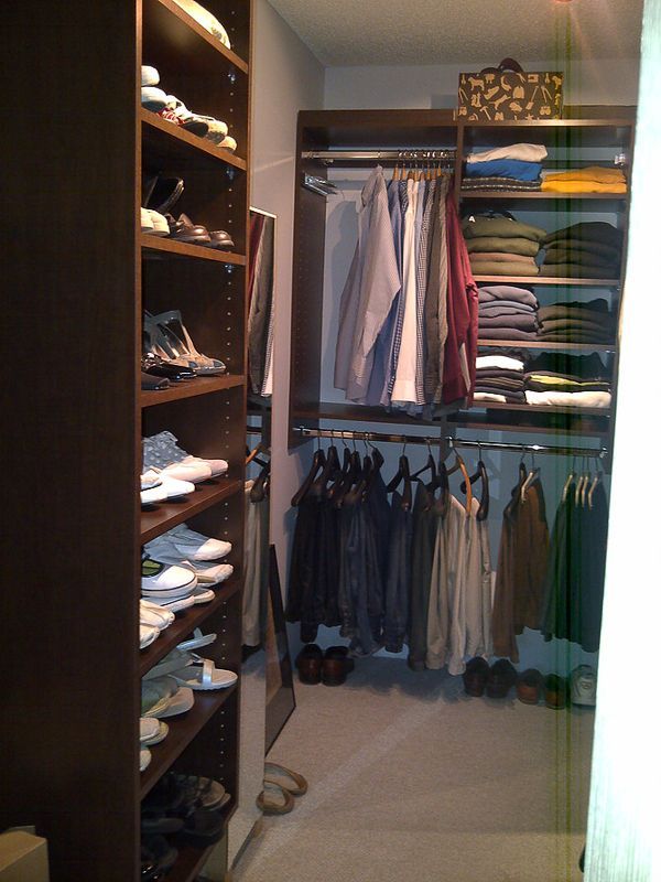 Small walk-in closet with hanging clothes, shelves, and folded items in neutral colors.
