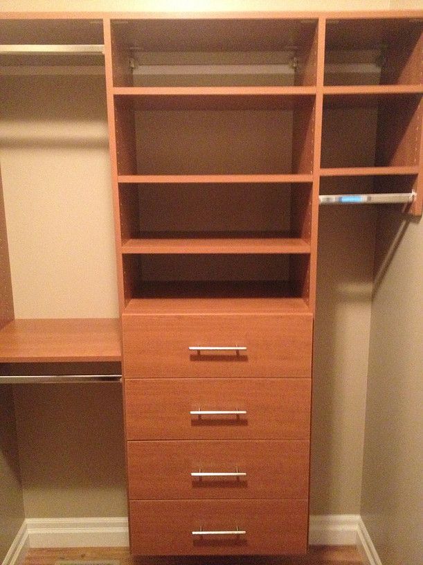 Built-in wooden closet organizer with shelves, drawers, and hanging space in a beige room.