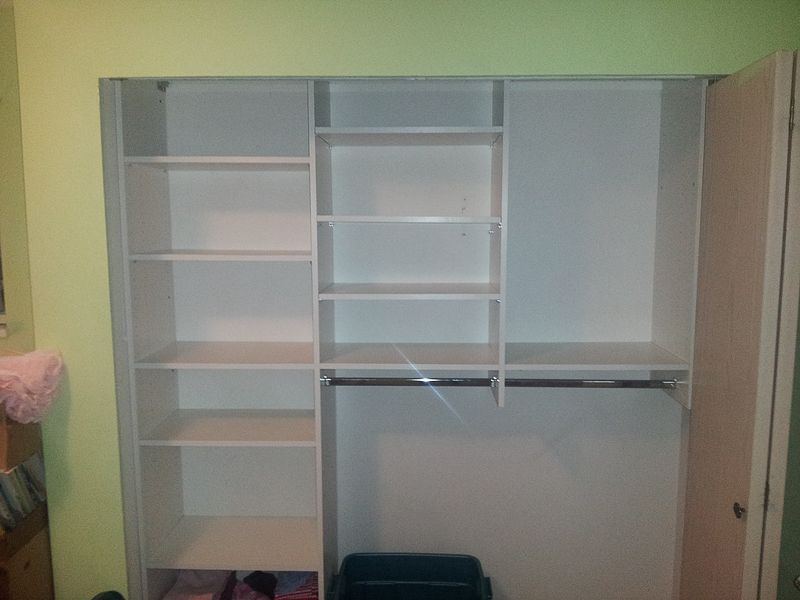 Built-in white closet with shelves, hanging rod, and open doors against a green wall